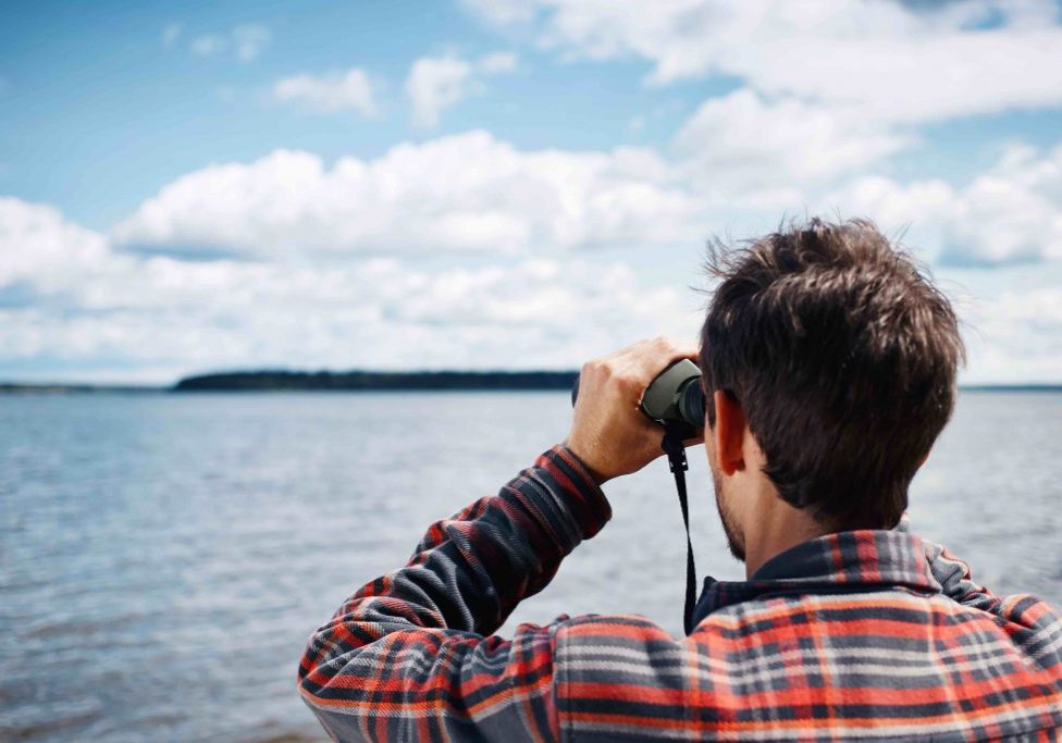 Close up back portrait man looks through binoculars while fishing at the lake on vacation